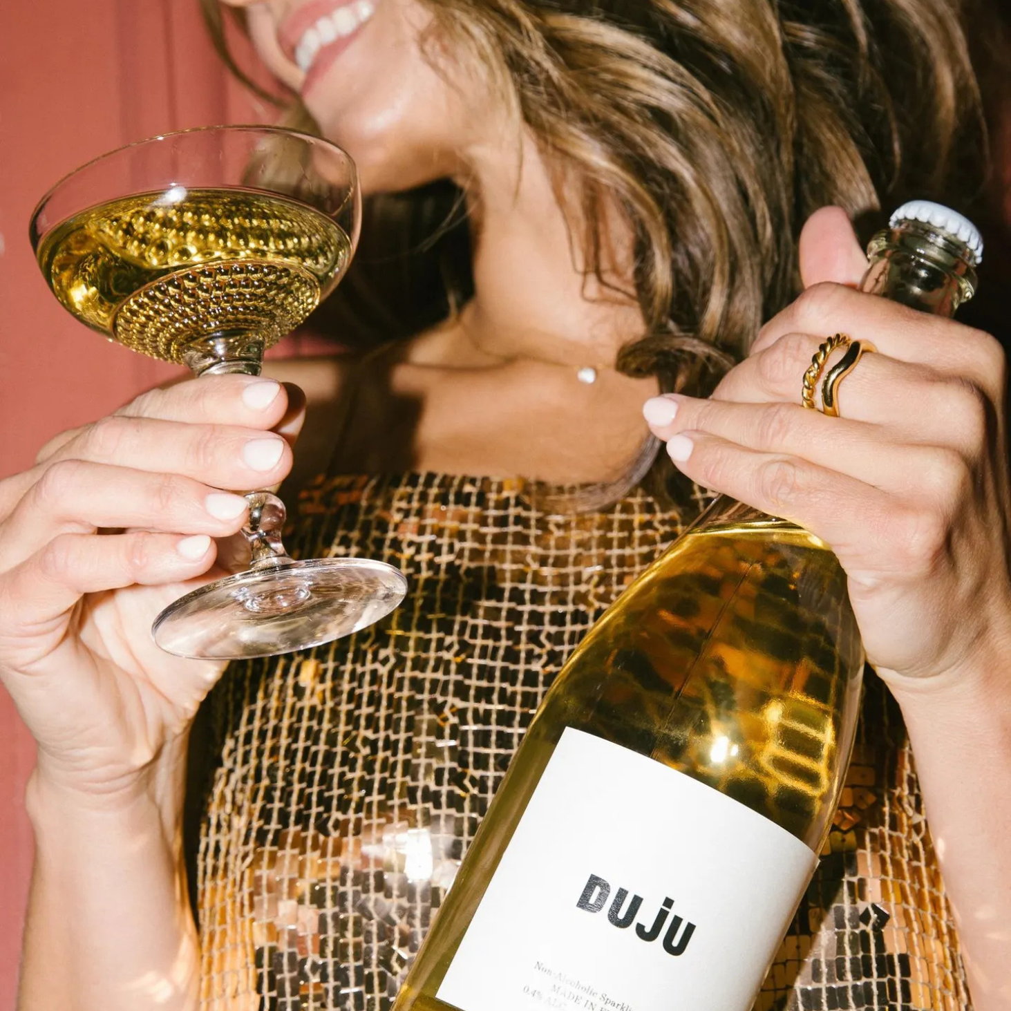 Woman holding a glass of white wine and a bottle labeled 'DUJU' against a pink background