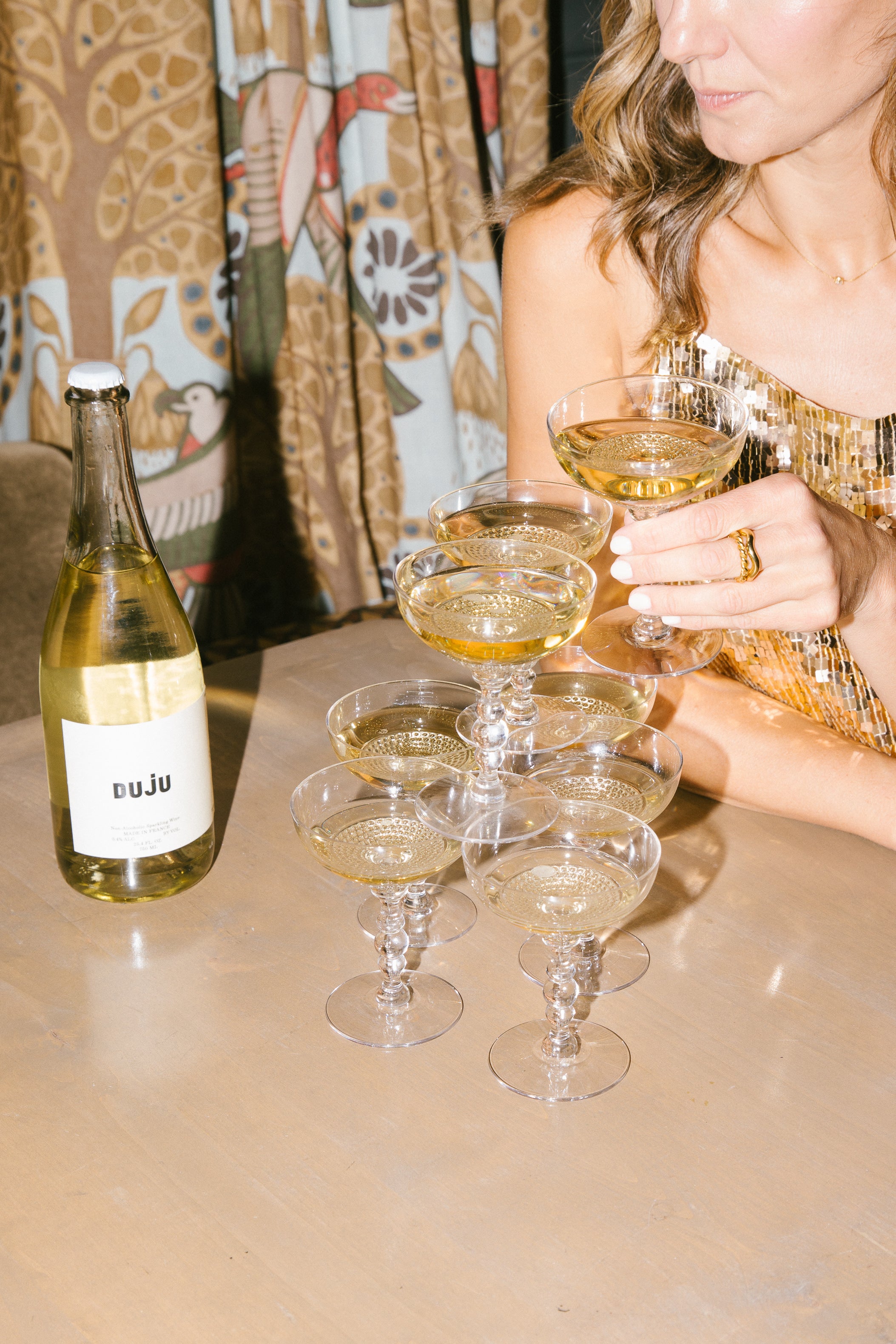 Woman holding a glass of white wine with a bottle labeled 'luJu' on a table.